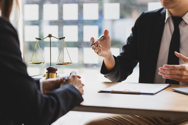 Two people in an office reviewing paperwork with the scales of justice sitting on the desk